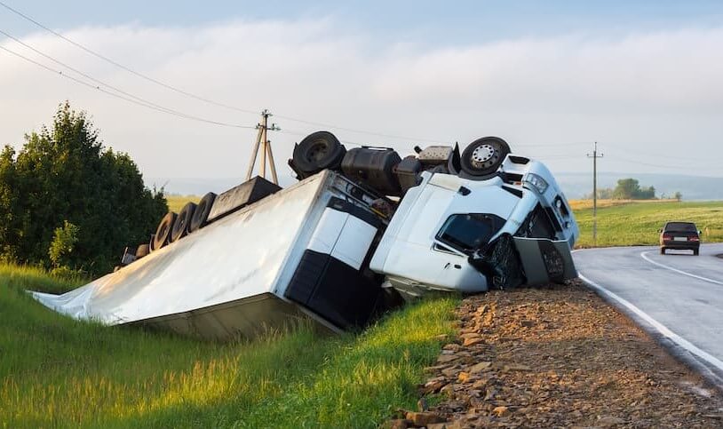 A truck in an accident lies in a ditch by rural road at daytime